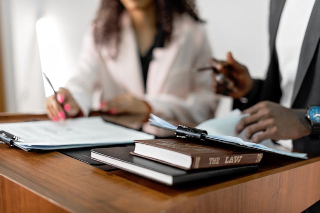 A law book and clipboards on a desk with two people blurred in the background
